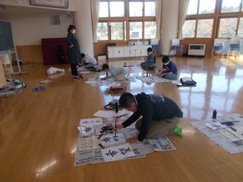 広い教室内で床に新聞紙をひき子供たちが習字をしている様子を写した写真