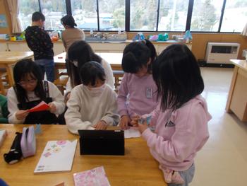 女の子がタブレットの周りに集まりながら動画をみている様子を写した写真