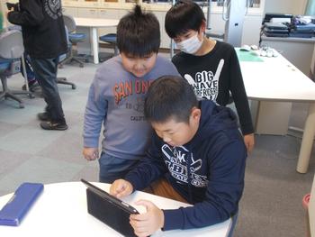 1人の男の子がタブレットを操作している様子を後ろから男の子2名が覗き込んでいる写真