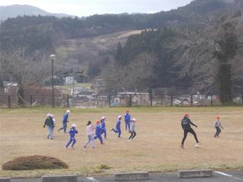 赤や白の帽子をかぶり、青の体操服やジャージを着た子供たちが広い校庭で運動している様子を写した写真