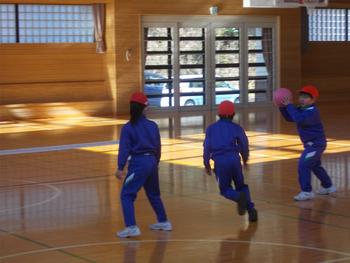 青いジャージに赤い帽子をかぶった児童3名がプレルボールを行い一番右の児童がボールを投げようとしている写真