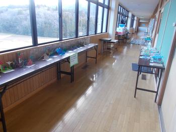 廊下に設置された両側のテーブルに、児童の工作作品がずらりと並べられている様子を写した写真