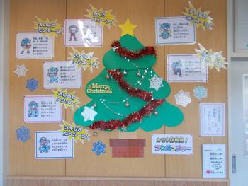 中央に大きな手作りのクリスマスツリーが貼られツリーの周りには、冬休みの過ごし方や注意点について書かれた掲示物が並んでいる学校内の掲示板を正面から写した写真