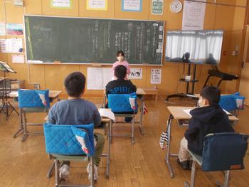 文字が書かれた黒板の前で女の子がほかの児童に説明をしている写真