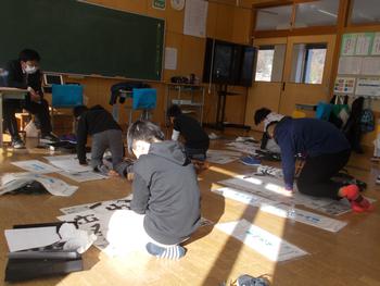 床に紙を置いて書き染めをしている生徒たちの写真