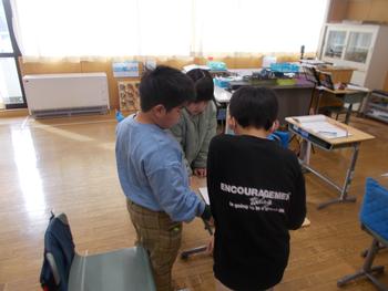 3人の児童が1つの机を囲んで立ち、協力して課題に取り組んでいる様子の写真
