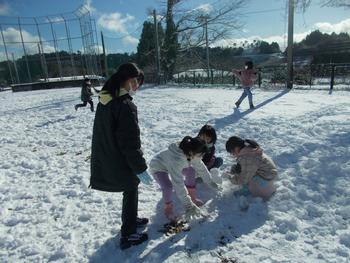 青空の下、一面に雪が積もった広場で雪遊びを楽しむ児童たちの写真