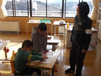 教員が近くで見守る中児童2名が机を囲み、教科書やプリントを使って学習をしている写真