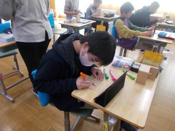 机に向かった生徒たちが思い思いにタブレットや色鉛筆を使い、オルゴールの制作活動に取り組む様子を撮影した写真