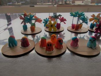 木製の台座の上に繭染めされた繭で作られた花瓶と花、そして可愛らしいキャラクターたちが並べられた、小学生の作品の写真