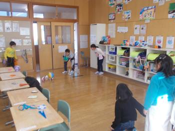 小学生たちが教室の床に散らばったボールを拾い集めたり、それを眺めたりしながら遊んでいる様子の写真