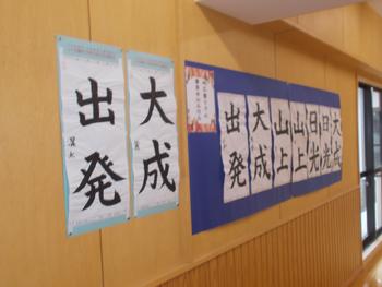 体育館の壁に「出発」や「大成」といった力強い文字が書かれた書道の作品が展示されている写真