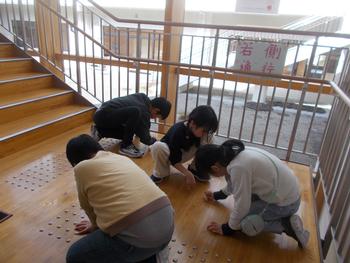 学校の階段の踊り場で複数の子供たちが床にしゃがみ、丁寧にすみずみを掃除している様子を写した写真