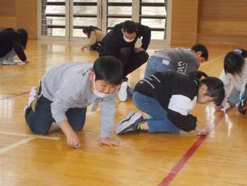 体育館の床にしゃがみ込み、スポンジを手に真剣に床を磨いている様子の児童たちと先生を捉えた写真