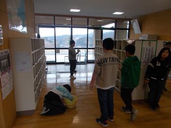 靴箱が並んだ学校の廊下で、複数の生徒がバケツやモップを使って清掃活動をしている様子の写真