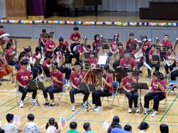 竹崎高級中学校56名がエンジ色の同じTシャツを着て楽器を演奏する姿をメインに写した写真