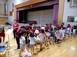 体育館で竹崎高級中学校の生徒と台湾国旗の小旗や風船を持った児童が縦一列になり話をしている様子の写真