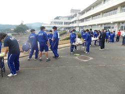 白い煙が漂う校舎前のスペースに長机などが置かれ、ジャージ姿の生徒たちがグループに分かれて活動している様子の写真