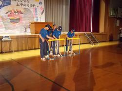 ステージの前でおそろいのユニフォームを着た4人の生徒が、2つ並んだ枠の後ろに立ち作業をしている写真