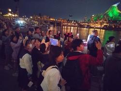テーマパークの夜のショーを見るために、多くの来場者が水辺に集まり、賑わっている様子の写真