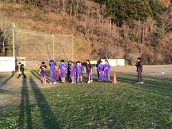 芝生のグラウンドに集まったジャージ姿の生徒たちが、赤いコーンの手前に並んで立っている写真