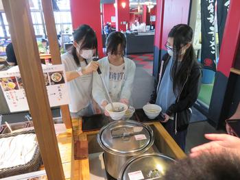 バイキングコーナーでマスクをつけた女子児童たちがスープを盛り付け、食事の準備をしている様子の写真