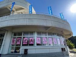 図書室の窓に「有終之美～あふれる才能を燃やし尽くせ～」と大きく書かれた文字が貼られ、屋上には青い旗が並んでいる写真