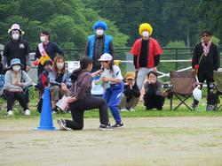 運動場の一角で、青いコーンの近くに一人の児童と片膝をついた関係者の女性が向かい合いっている借り物競争での写真