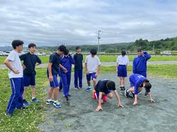 クラウチングスタートのポーズをとっている生徒2人の後ろに体操着を着た生徒たちが集まっている写真