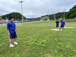 芝生の広場で砲丸投げの練習をしている3人の生徒の写真