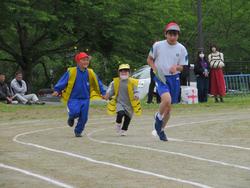 赤い帽子をかぶった男子児童が1番前を走り、黄色いベストを着た2人の児童が手をつないで並んで走っている借り物競走での写真