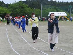運動場のトラック上を、保護者の方々と児童たちが整列し踊りを踊りながら歩いている写真