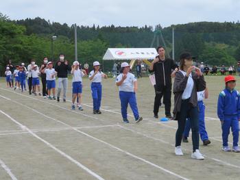 保護者と児童がトラックをぐるりと並んで踊りを踊っている写真
