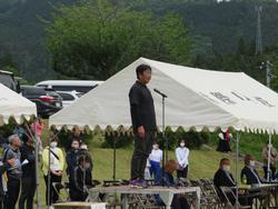運動会の閉会式で、演台の上に黒い服を着た男性が立ち、マイクに向かって話している様子の写真