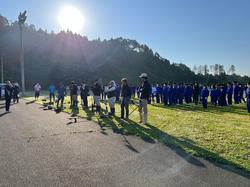 朝日を背にして広場に集まった大勢の、保護者と運動着姿の生徒たちが、列になって並んでいる様子を写した写真