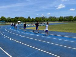 青い陸上トラックを複数の生徒が列になって走っている写真