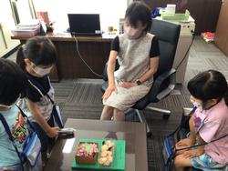 机の上に置かれた立派な装飾のある箱を囲み、座っている女性の説明を聞きながら子どもたちが熱心に見ている様子の写真