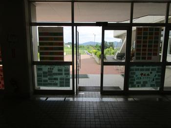 昇降口のガラス扉に、メッセージを書いたカードがたくさん貼られた白と水色の模造紙が複数枚掲示されている写真