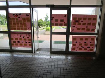 昇降口のガラス扉に、メッセージを書いたカードがたくさん貼られたピンク色の模造紙が複数枚掲示されている写真