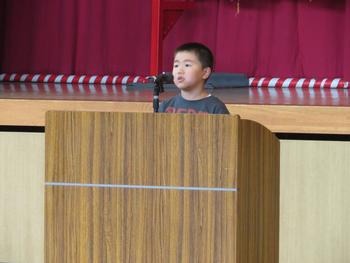 演台に立ちマイクを使って話をしている男の子の写真