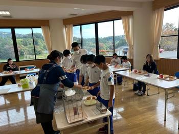室内に長机が設置され中央に給食を取りに来ている子供達と座ってまっている保護者の方の写真