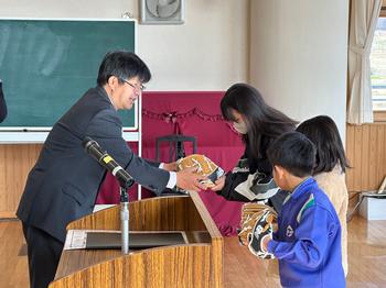 3人の児童が並んで校長先生からグローブを受け取っている写真