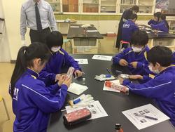 教室で、マスクと体操服を着用した生徒たちが、グループに分かれて黒いテーブルを囲み、実験道具を使い学習している写真
