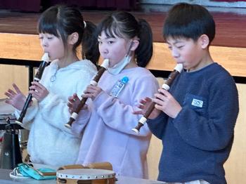 舞台の前で3人の児童が一生懸命リコーダーを演奏している様子を捉えた写真