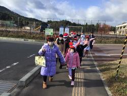 冬の装いで防寒着を着た5年生と1年生が手をつないで道路脇の歩道を列になって歩いている写真