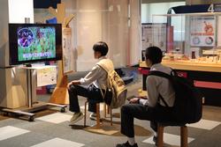 制服姿の男子生徒二人が室内に置かれたモニター前の椅子に座って、モニターに映る映像を真剣に見ている写真