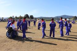 運動場で、赤い鉢巻を頭に巻いた生徒たちが車いすの生徒も交えて円になり、玉入れの準備をしている写真