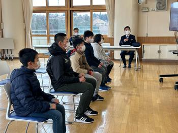 教室中央に並べられた椅子に座った児童たちが、前を向いており、生徒たちの横に置かれたテーブルに佐藤署長と男性が座っている写真