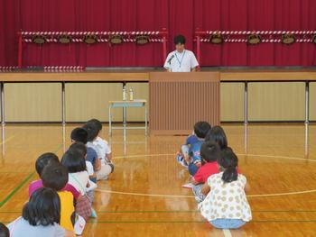 2列に並んで座りながら前方の先生の説明を聞いている子供たちを体育館の後方から写した写真