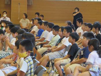 体育館内のパイプ椅子に座り説明を聞いている子供たちの写真